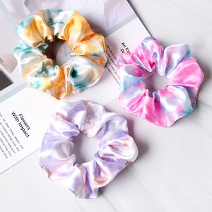 Close-up of three tie-dye satin scrunchies with silky texture on marble background