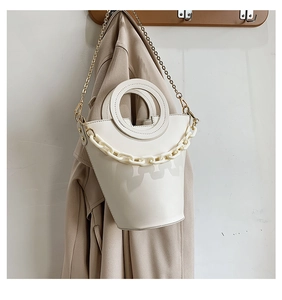 Detail of white bucket bag with circular handle and acrylic chain on a trench coat