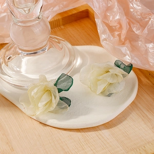 Detailed shot of cream fabric rose earrings with green leaves on a white tray