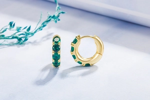 Detail view of gold hoop earrings with multi-prong set emerald green zircons on blue floral backdrop