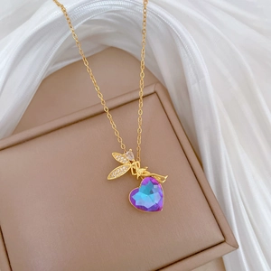 Macro view of gold angel pendant with blue and purple heart crystal on beige velvet box