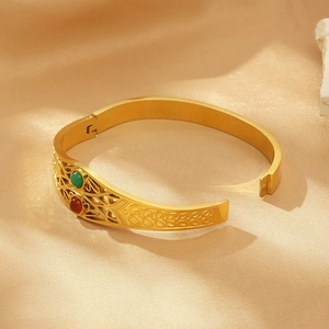 Detailed view of hollowed-out gold bangle with red and green beads on champagne silk