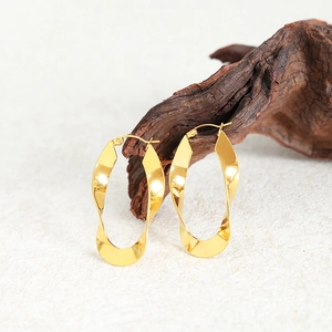Polished gold U-shaped twisted hoop earrings displayed on a rustic wood stand