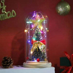 Close-up of glass dome Christmas tree with LED lights and red velvet bow on wood base