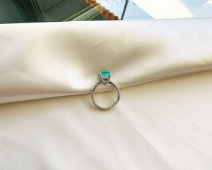 Detailed macro view of an emerald cut green gemstone ring on a beige silk fabric