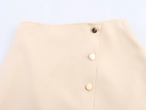 Detail of beige skort waist featuring three decorative gold buttons and asymmetric hem design