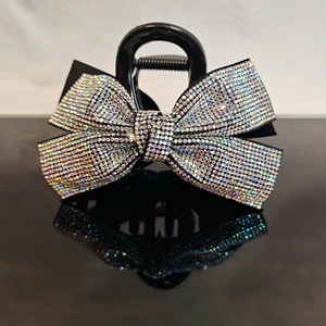 Close-up of black bow hair claw clip with colorful rhinestones on reflective surface
