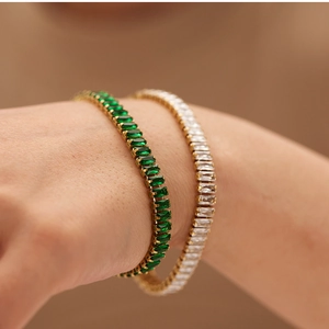 Close-up of gold tennis bracelets with green and white cubic zirconia on a model's wrist