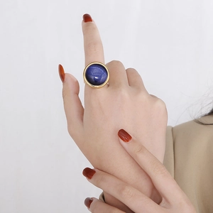 Macro detail of a large round blue gemstone ring with gold plating on a model hand