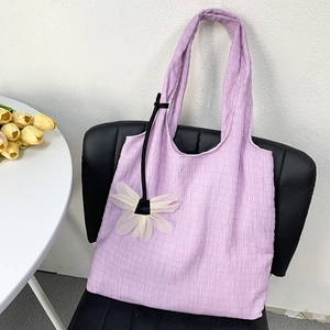 Close-up of light purple pleated canvas bag with white flower charm on a leather chair