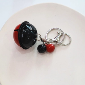 Detail of red and black enamel bell keychain with silver-colored ring on ceramic plate