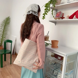 Sac fourre-tout en toile à fleurs rose et vert porté par un mannequin en café