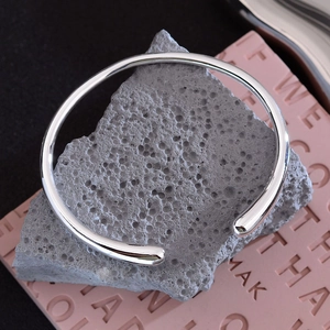 Minimalist silver open teardrop bangle with polished metal finish on a textured stone