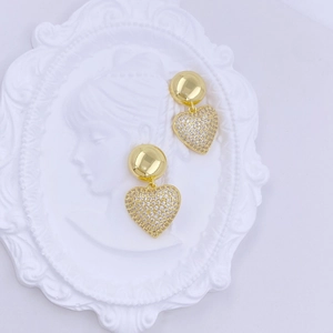 Close-up of elegant gold heart earrings with white crystals on a white relief background