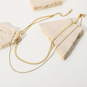 Double-layered gold snake chain and cable chain necklace displayed on stone props