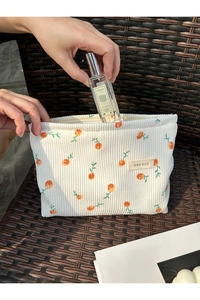 Detail of hand placing perfume into white corduroy makeup bag with floral pattern