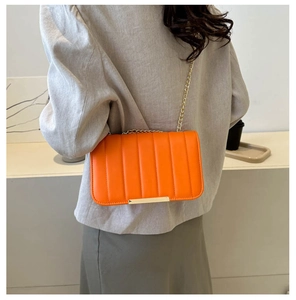 Close-up of orange quilted crossbody bag with gold chain strap on a beige blazer