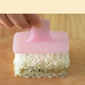 Pink sushi mold with a top handle pressing rectangular rice on a light wood surface