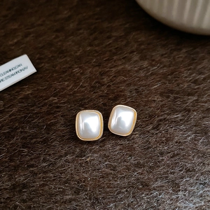 Gros plan de boucles d'oreilles perles carrées avec monture dorée sur fond de peluche