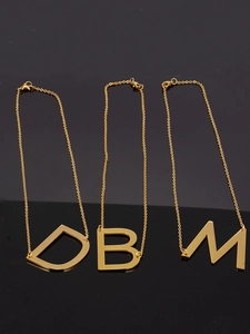 Detailed view of 18K gold plated stainless steel letter pendants D, B and M on black background