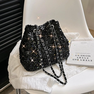 Elegant black sequin bucket bag with metal chain strap displayed on a white chair