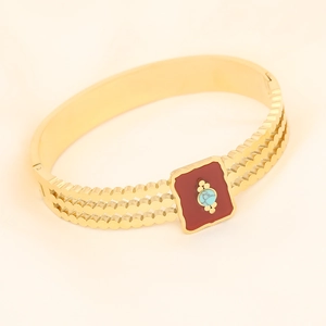 Detail of golden wavy bracelet featuring a red square inlay with a turquoise center stone