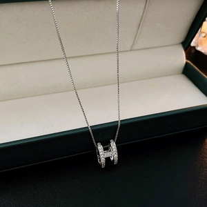 Macro shot of a silver H pendant necklace with zircons in a green velvet box