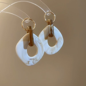 Macro detail of geometric earrings featuring marble resin resin and gold metallic rings