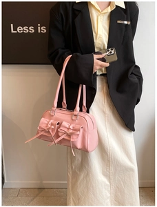 Détail du sac à main en cuir verni rose avec nœuds décoratifs et poches frontales