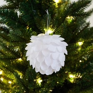 White petal textured Christmas ball ornament hanging on a pine tree with warm lights