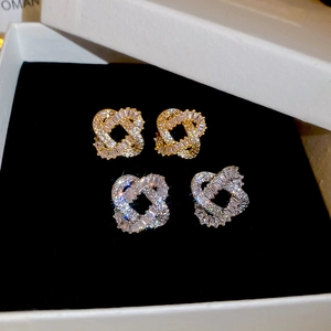 Detailed view of silver and gold plated knot stud earrings with cubic zirconia in a box