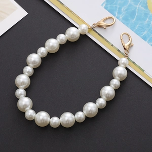 Detail of white gradient pearl phone chain with gold metal clasps on a black surface