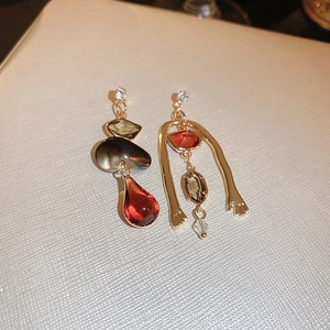 Dettaglio di orecchini asimmetrici vintage con cristalli bordeaux e finitura oro