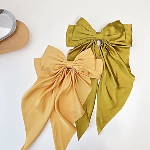Detail view of large golden and moss green silk satin bow hair clips with long streamers