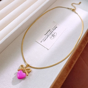 Détail macro d'une chaîne serpent dorée avec pendentif cœur rose et nœud doré