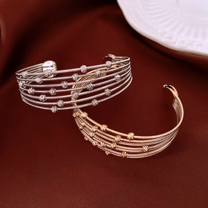 Detail view of multi-layer beaded open bangles in gold and silver on silk fabric