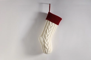 Detail of cable knit Christmas stocking with ivory body and deep red cuff hanging on a wall