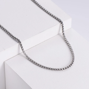 Macro detail of high-shine silver box chain necklace on minimalist white display stand