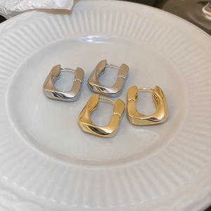 Détail de boucles d'oreilles en U torsadées en or et argent sur céramique blanche