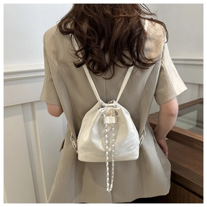 Rear view of a white PU leather bucket backpack with chain straps on a female model
