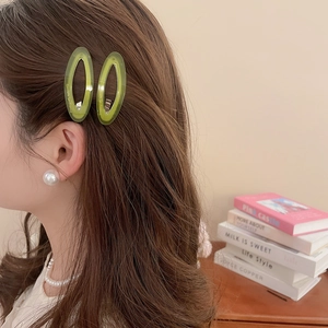 Close-up of translucent green acetate oval hair clips and pearl jewelry on a model
