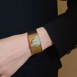 Detailed view of wide gold cuff bracelet featuring pearl flower cluster on wrist