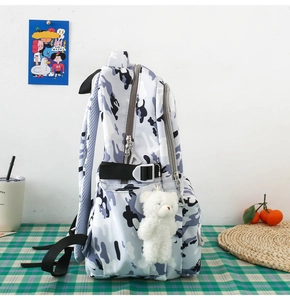 Detail of camouflage backpack featuring side pocket, adjustable strap and plush bear charm
