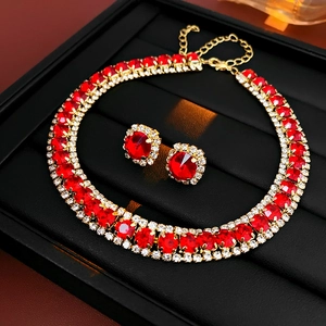 Macro shot of gold necklace and earrings set with red gemstones on black tray