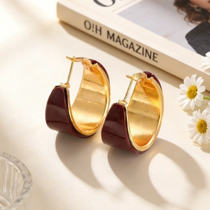 Detail of wide C-shaped gold hoop earrings with premium deep red enamel finish