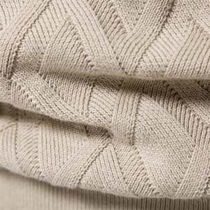 Macro view of beige cotton knit sweater showing intricate diamond and cable textures