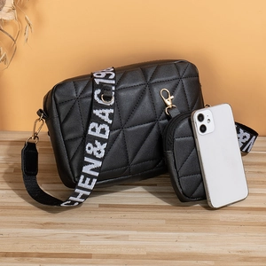 Sac bandoulière matelassé noir avec sangle large et mini pochette sur table en bois