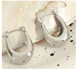 Macro shot of silver U-shaped chunky hoop earrings on a decorative shell and ceramic tray