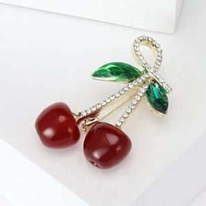Charming red cherry brooch with sparkling rhinestones and gold accents on a white base