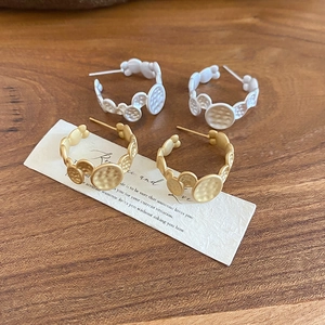 Close-up of gold and matte silver C-shaped metal earrings with hammered texture on wood